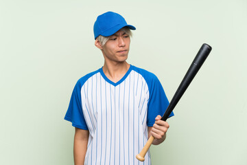 Wall Mural - Young asian man playing baseball over isolated green background with sad expression