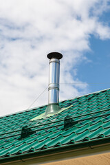 Stainless steel metal chimney pipe on the roof of the house against the sky.