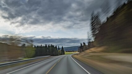 A drive to the arctic circle in Norway. The road is going through the rural landscape, forests and fields stretch on both sides. Traffic is low. Gray clouds hanging above.