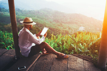 Hipster guy is holding touch pad with copy space on the screen for your advertising text message or information content. Man is watching video on digital tablet that he just shot during trip in Asia