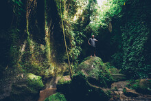Experienced Male Tourist Exploring Wild Areas Of Tropical Forests During Summer Trip In Asia Jungle.Young Man Hiker Standing On Big Stone In Wood Forest Enjoying Green Vegetation And Environment