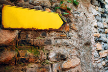 Yellow Arrow Sign On Old Stone Brick Wall. Direction Pointer With Empty Copy Space.