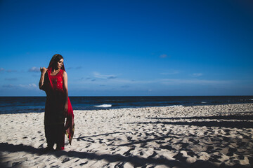 Beautiful Sikh model wearing traditional red clothing on tropical beach with waves in background 