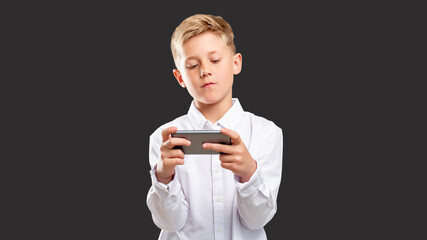 Mobile game addiction. Online entertainment. Confident boy playing on smartphone isolated on dark background.