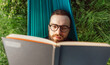 © mykolastock - Bearded stylish young hipster male reading book and lying in hammock