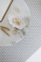 Wall Mural - Minimal fashion composition with golden earrings in seashell on marble table with mirror and wheat stalks. Flat lay, top view bijouterie / jewelry concept on mosaic tile background.
