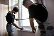 Two professional workers in uniform using tape measure while measuring window and making notes for installing blinds indoors. Construction and maintenance concept