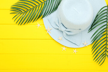 Poster - Summer straw hat with green palm leafs on yellow wooden background