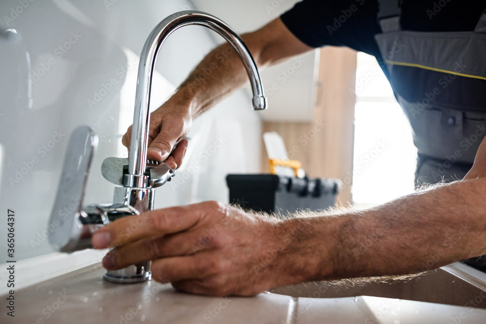 Close up of hands of aged repairman in uniform working, fixing broken kitchen tap using adjustable wrench. Repair service concept