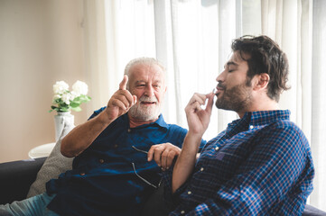 An adult hipster son and senior father talking on sofa at home, family concept