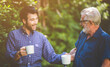 © chokniti - senior father and adult son with coffee cup talking in the garden at home, relax morning time