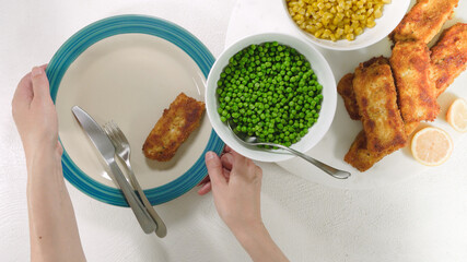 Wall Mural - Golden batter deep fried fish fillet, served with green peas, sweet corn, and slices of lemon close up on a plate on white background