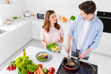 Top above high angle view photo of two people spouses man woman have dream chef cuisine weekend man hold spatula frying pan yummy barbecue meat girl want serve plate in kitchen house indoors