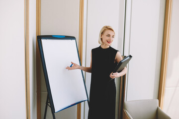 Positive female marketing expert dressed in formal outfit making speech on presentation satisfied with successful project; attractive businesswoman having conference meeting explaining working plan