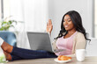 © Syda Productions - remote job, technology and people concept - happy smiling african american young woman with laptop computer having video call at home office and resting her feet on table
