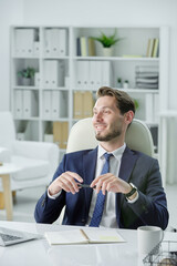 Poster - Smiling handsome businessman with stubble sitting at desk and listening to business partner while meeting with him in office