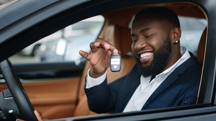 Closeup businessman shaking key in new car. African man smiling in vehicle