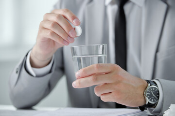 Poster - Close-up of unrecognizable businessman in wristwatch dissolving pill into water while suffering from morning hangover at workplace