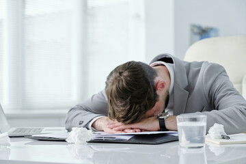 Poster - Exhausted young businessman lying on table with papers and crumpled napkins while suffering from headache