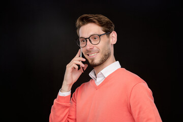 Poster - Smiling confident young man in bright sweater having phone conversation against black background