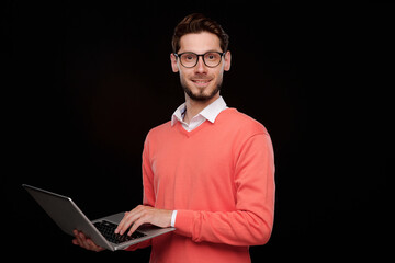 Poster - Portrait of content confident young IT specialist with stubble standing against black background and using modern laptop