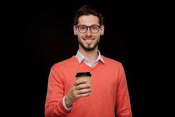 Poster - Portrait of positive young man in orange sweater drinking coffee to go against black background