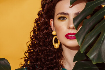 Close up summer fashion portrait of beautiful curly woman with fuchsia color lips, yellow eyes makeup, wearing big trendy earrings, posing on yellow background. Copy, empty space for text