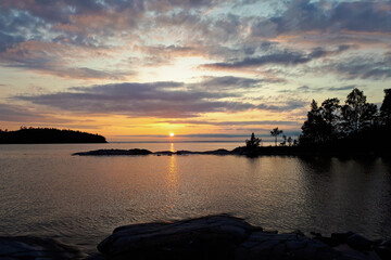 Wall Mural - The sun goes over horizon, a beautiful sunset over the lake, clouds in the blue sky. Horizontal photo of calm nature