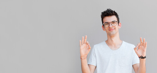Wall Mural - Portrait of a cheerful young man showing okay gesture isolated on the gray background