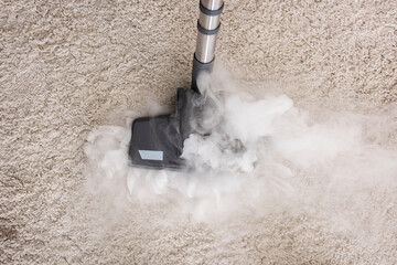 Top view of brush of vacuum cleaner with hot steam on carpet at home