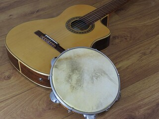 Wall Mural - Close-up of an acoustic guitar and a pandeiro (tambourine), a Brazilian percussion musical instrument, on a wooden surface. They are widely used to accompany samba and choro music.