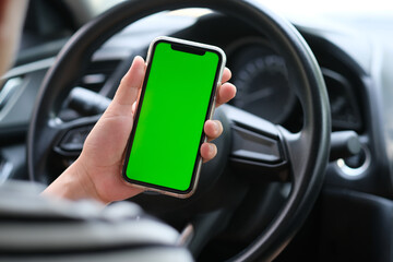 Wall Mural - over shoulder of man holding green screen smart phone inside car. blur background