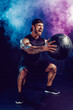 © zamuruev - Aggressive bearded muscular sportsman is working out, push up with a medicine ball isolated on dark studio background with smoke.