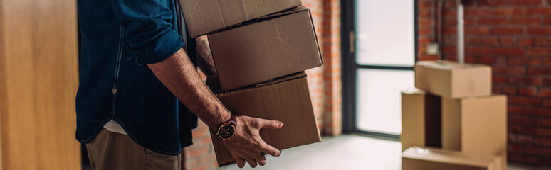 panoramic crop of businessman holding boxes and moving in new office