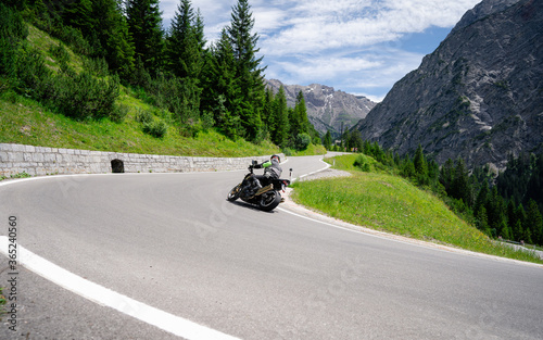 Obraz Dibond Motorcycle driver riding in Alpine road, Austria, Europe. Outdoor photography, mountain landscape. Travel and sport photography. Speed and freedom concept