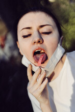 Close-up Of Young Woman Wearing Mask Sticking Out Tongue With Covid 19 Text