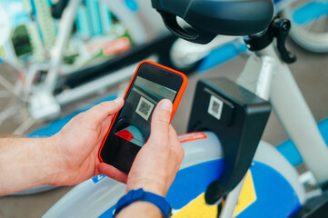 Close photo, man scans a smartphone QR code on a bicycle. Bicycle sharing in a mobile application. Bicycle rental for walking. Background. Sharing concept.