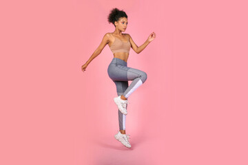 sporty woman practicing squat exercises in studio. african woman in sportswear working out on pink b