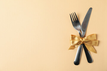 Cutlery with bow on beige background, space for text