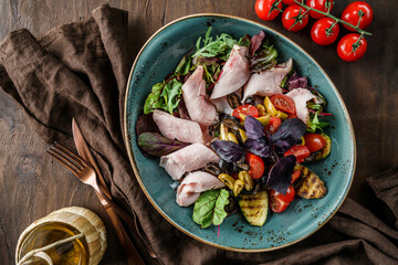 Wall Mural - Delicious salad with sliced of turkey ham, grilled zucchini, tomatoes, basil, greens, olives and oil in bowl on wooden background. Healthy food, dieting, Buddha bowl, top view