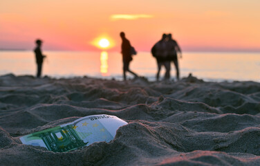 Two guys, a man and a boy looking for a lost 100 euro banknote against the background of a sea sunset