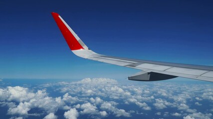 Wall Mural - Airplane flight. Wing of an airplane flying above the clouds with blue sky. View from the window of the plane.