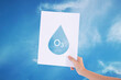 Female hands holding white paper with water drop in blue sky background./Ozone concept
