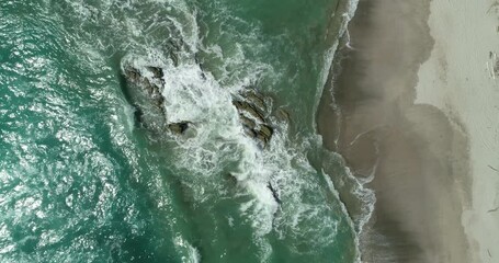 Wall Mural - Aerial top view of ocean blue waves break on a beach. Sea waves and beautiful sand beach aerial view drone shot. Bird's eye view of ocean waves crashing against an empty sand beach from above.