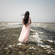 Teenage Girl Covering Her Face With Long Hair While Standing On Beach