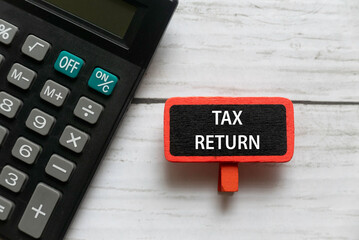 Top view of calculator and red tag written with TAX RETURN on white wooden background.