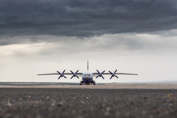 Wall Mural - Front view of four propeller airplane. Big heavy gross weight airliner standing on airport apron, dynamic dark grey cloudy sky background. Huge freight aircraft for air cargo transportation.