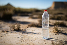 Unlabeled Plastic Water Bottle On Arid Soil Into Desertic Landscape With Copy Space