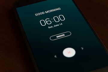 On a black smartphone, an alarm clock rings for 6 am with the inscription Good morning close-up, background