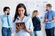 © Daniel Ernst - Latin american businesswoman working at tablet with international team in background